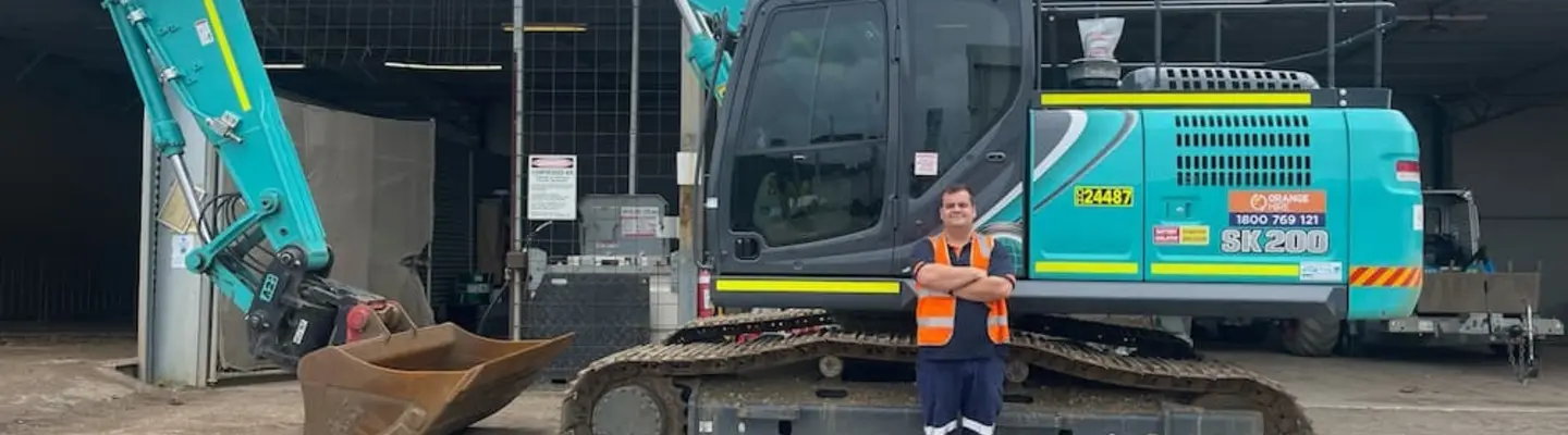 A man standing beside an excavator near installed safety barriers on a job site.