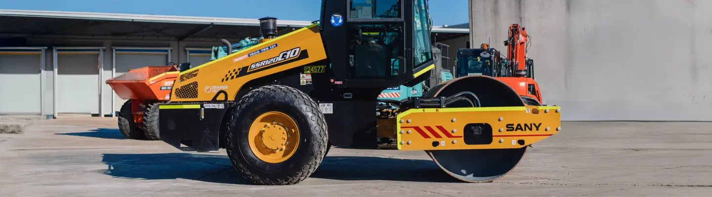 Standby compaction roller parked near construction barriers, ready for ground stabilization work on the site.