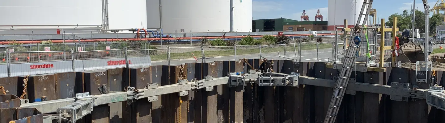 Construction worker installing hydraulic bracing systems in a trench to prevent wall collapse and enhance excavation safety.