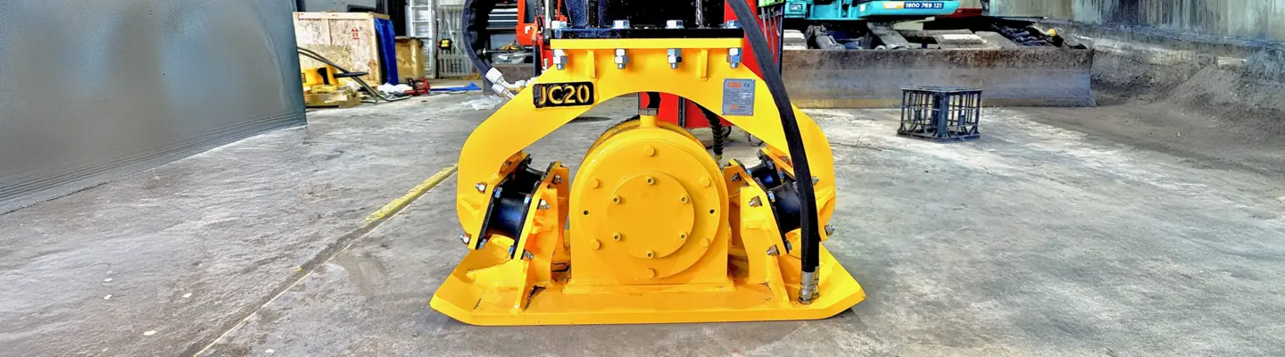Plate compactor machine on a construction site near safety barriers, used for compacting soil and maintaining ground stability.