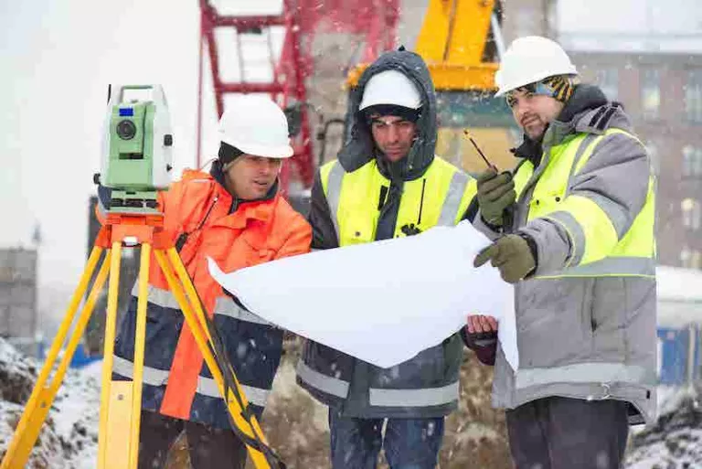 workers looking at blueprints in the winter wearing hard hats and safety vests
