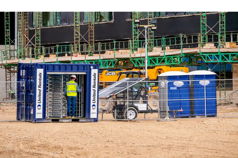 A worker using a turnstile to enter a jobsite on the left and porta potties on the right.