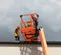 Side view of an orange aerial lift platform with a worker standing next to it inspecting the roof edge on building exterior.