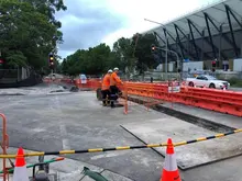 Workers standing in front of installed water-filled safety barriers along a roadside construction zone.
