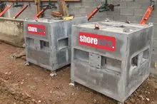 Worker setting up a concrete counterweight system to stabilize poles during a propping job on a construction site.