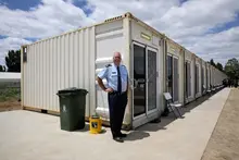 Man standing confidently in front of a modern containerized house, showcasing innovative modular living design.