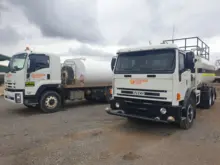 Two water carts parked at a construction site, used for dust suppression and safety compliance near temporary barriers.
